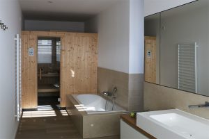 Masterbad mit Badewanne, Waschbecken, Spiegel und holzvertäfelter Sauna
